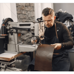 A man tailor busy in making leather clothes on sewing machine.