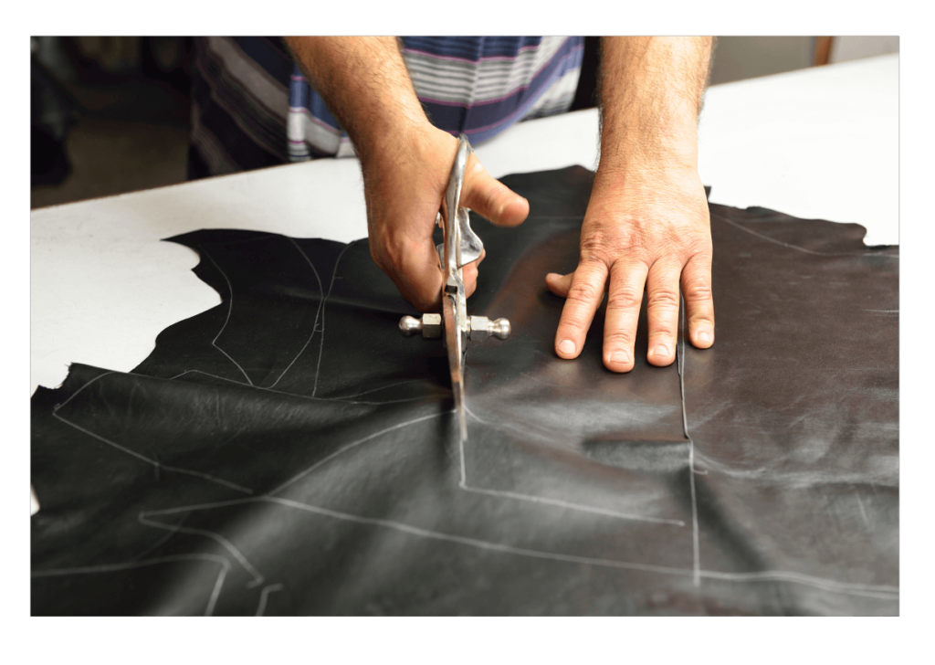 A man tailor cutting leather cloth with scissor as per measurement marks.