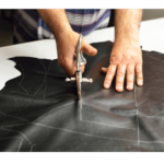 A man tailor cutting leather cloth with scissor as per measurement marks.